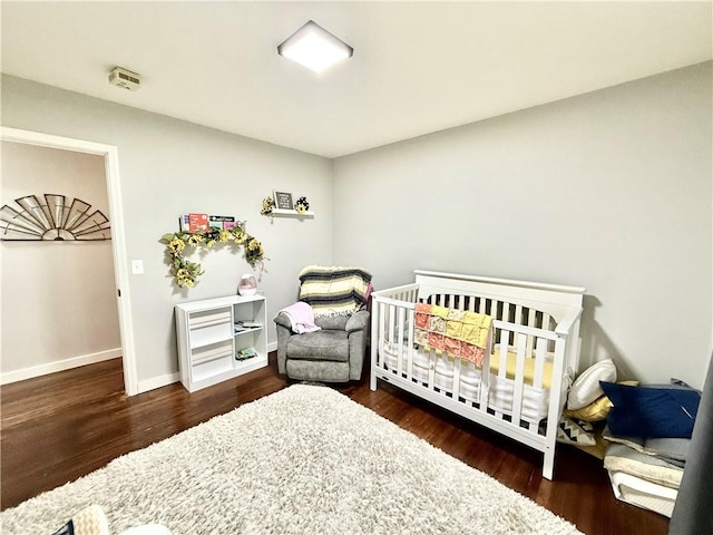 bedroom with baseboards, a crib, and wood finished floors