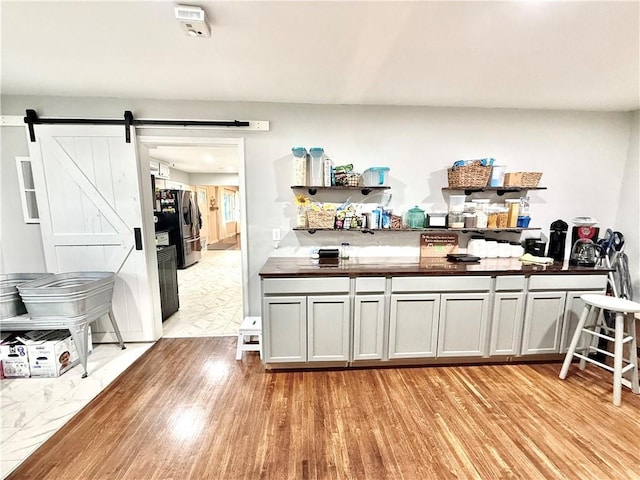 bar with light wood-style floors, a barn door, and freestanding refrigerator