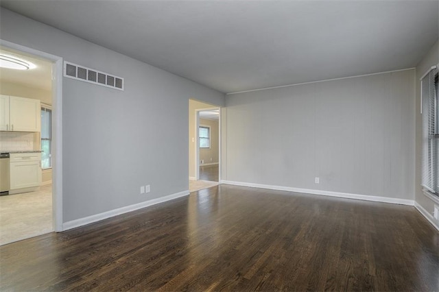 empty room featuring dark wood-style flooring, visible vents, and baseboards