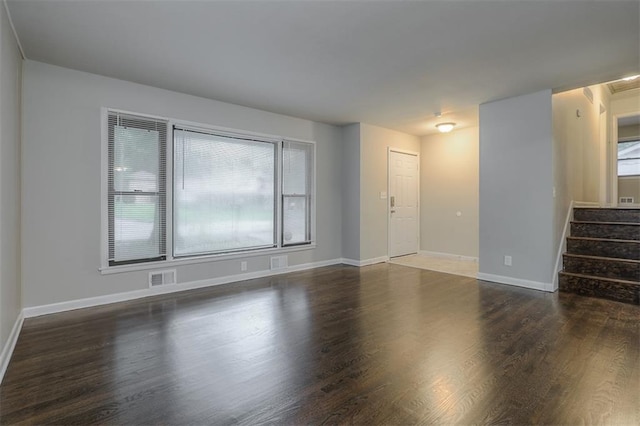 unfurnished living room with wood finished floors, visible vents, stairway, and baseboards