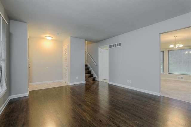 unfurnished living room with a notable chandelier, visible vents, stairway, and wood finished floors
