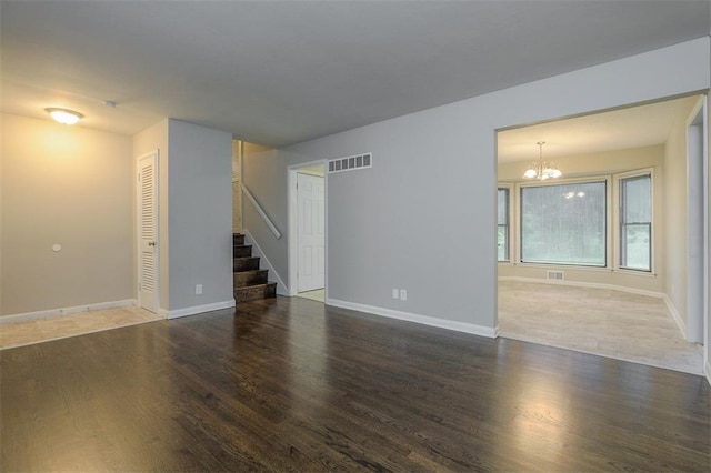 unfurnished living room with wood finished floors, stairs, a chandelier, baseboards, and visible vents