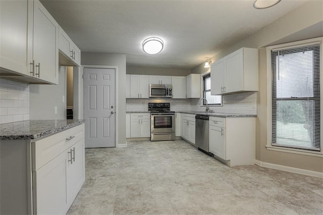 kitchen with a sink, tasteful backsplash, light stone counters, white cabinets, and appliances with stainless steel finishes