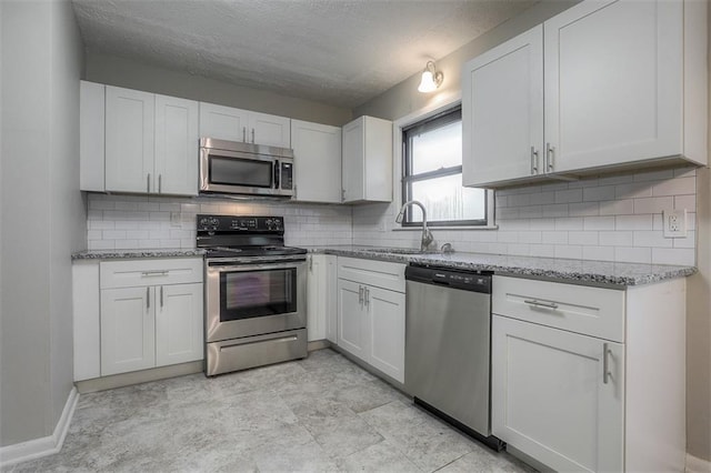 kitchen featuring light stone counters, white cabinetry, decorative backsplash, a sink, and appliances with stainless steel finishes