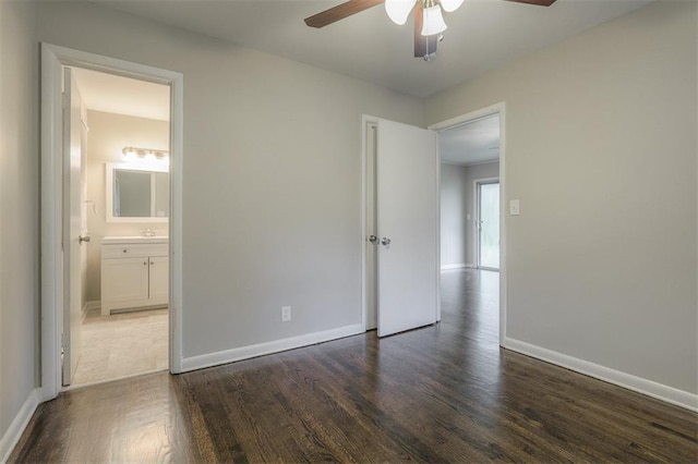 unfurnished bedroom with dark wood-style floors, ensuite bathroom, a ceiling fan, and baseboards
