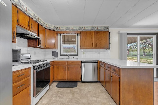 kitchen featuring stainless steel dishwasher, a peninsula, under cabinet range hood, range with gas cooktop, and a sink