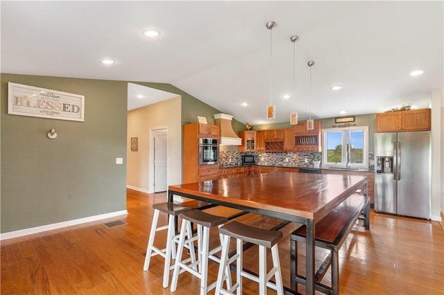 kitchen featuring hanging light fixtures, appliances with stainless steel finishes, brown cabinetry, tasteful backsplash, and custom exhaust hood