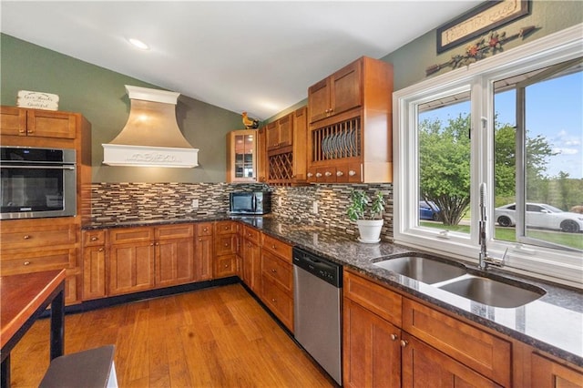 kitchen featuring brown cabinetry, decorative backsplash, wood finished floors, custom range hood, and black appliances
