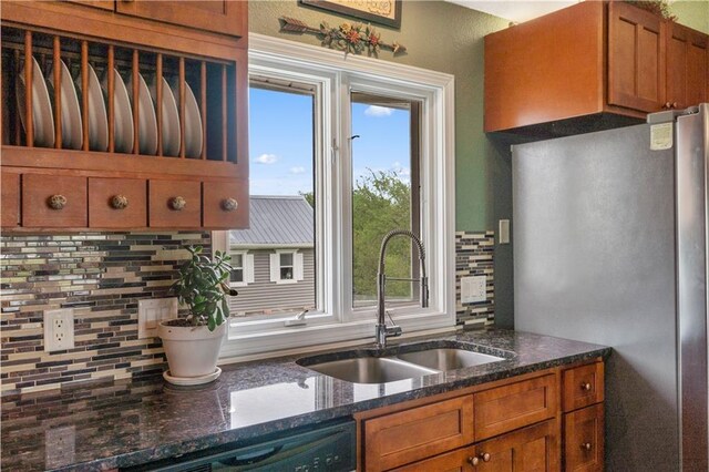 kitchen featuring tasteful backsplash, brown cabinets, dishwasher, a sink, and freestanding refrigerator