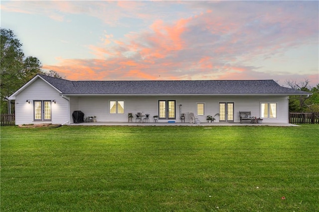 back of property at dusk with french doors, fence, a yard, and a patio area
