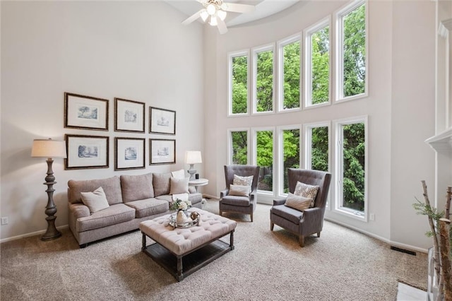 carpeted living area featuring a high ceiling, healthy amount of natural light, ceiling fan, and baseboards