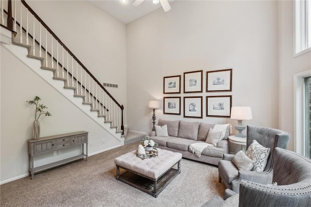 living area with a towering ceiling, carpet floors, stairway, a ceiling fan, and baseboards