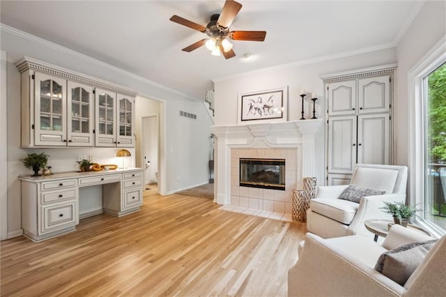 living area with ornamental molding, light wood finished floors, ceiling fan, a tile fireplace, and baseboards