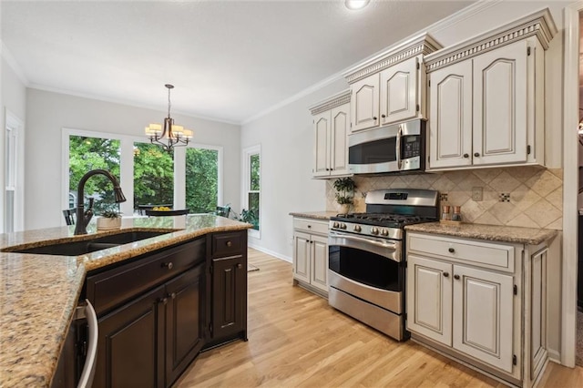 kitchen with appliances with stainless steel finishes, a sink, light wood-type flooring, tasteful backsplash, and crown molding