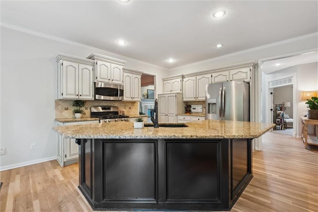 kitchen with appliances with stainless steel finishes, tasteful backsplash, light wood-type flooring, light stone counters, and an island with sink