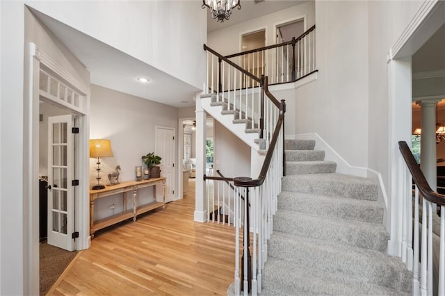 stairs with wood finished floors, a chandelier, baseboards, a high ceiling, and recessed lighting