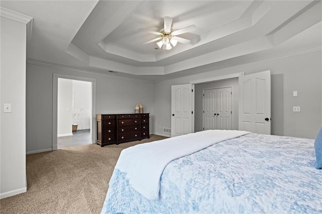 carpeted bedroom with a raised ceiling, crown molding, baseboards, ceiling fan, and ensuite bath