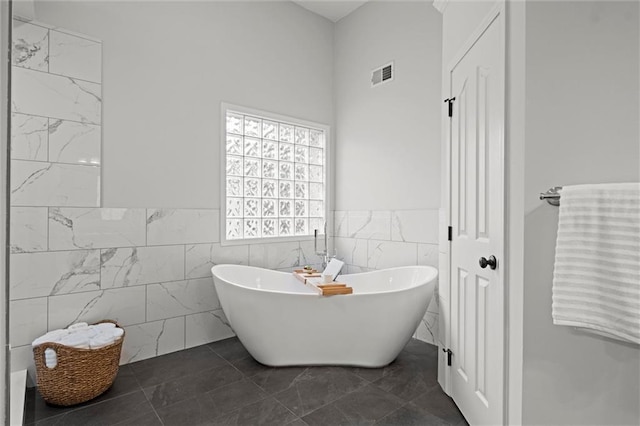 bathroom with tile walls, a soaking tub, a wainscoted wall, and marble finish flooring