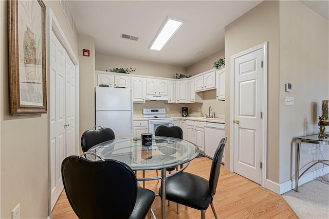 kitchen with white cabinetry, a sink, visible vents, under cabinet range hood, and white appliances