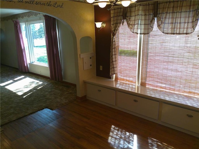 unfurnished dining area featuring arched walkways, baseboards, and wood finished floors