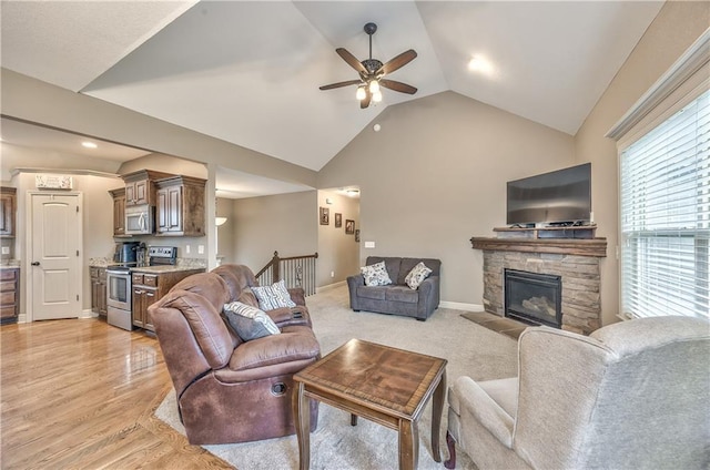 living area with lofted ceiling, a stone fireplace, baseboards, ceiling fan, and light wood-type flooring