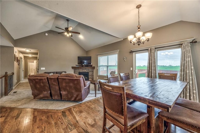 dining room with ceiling fan with notable chandelier, wood finished floors, lofted ceiling, and a fireplace