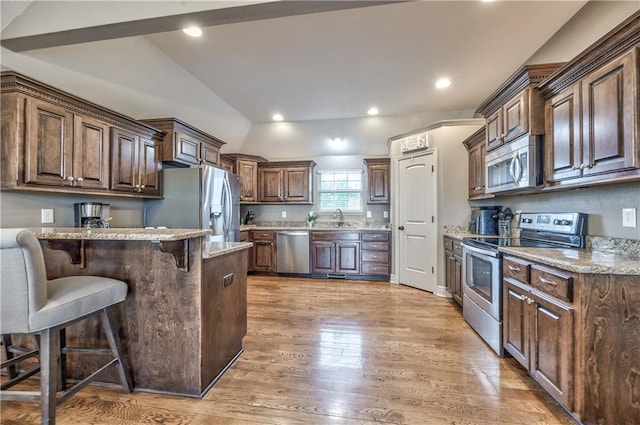 kitchen featuring a peninsula, lofted ceiling, a kitchen breakfast bar, light wood finished floors, and stainless steel appliances
