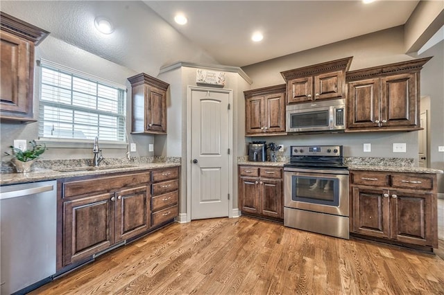 kitchen with stainless steel appliances, dark brown cabinets, a sink, and light wood-style floors