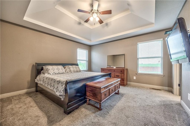carpeted bedroom with a ceiling fan, a tray ceiling, and baseboards