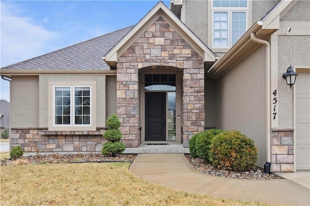 view of exterior entry with a yard, stone siding, stucco siding, and a shingled roof