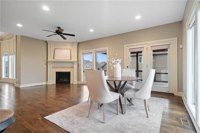 dining room featuring wood finished floors, a large fireplace, baseboards, a ceiling fan, and french doors