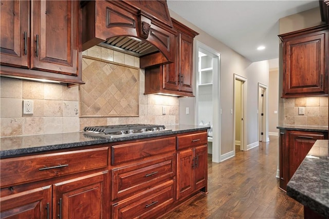kitchen with premium range hood, stainless steel gas cooktop, dark stone countertops, and tasteful backsplash