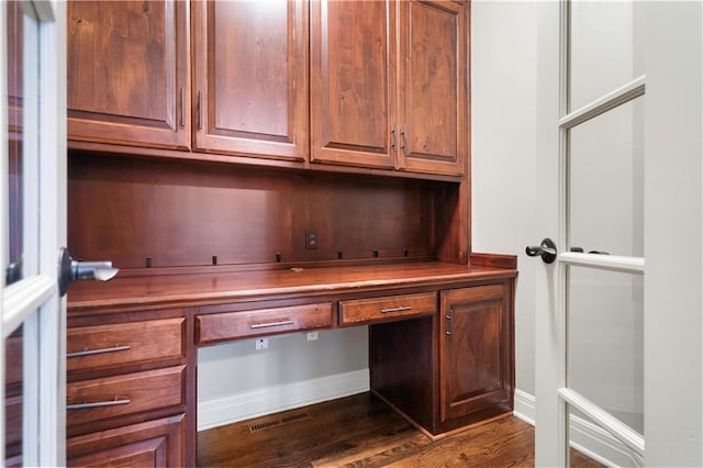 unfurnished office with visible vents, baseboards, built in desk, and dark wood finished floors