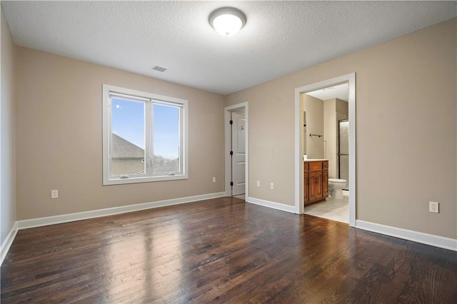 unfurnished bedroom with a textured ceiling, visible vents, wood finished floors, and baseboards