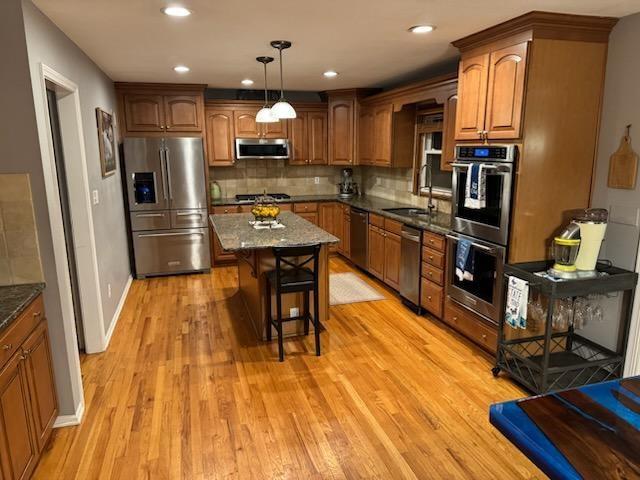 kitchen featuring a breakfast bar area, brown cabinets, tasteful backsplash, a sink, and appliances with stainless steel finishes