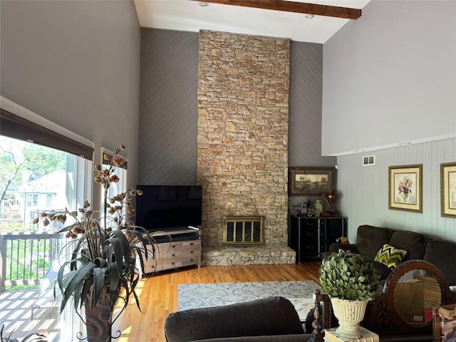 living area with visible vents, wood finished floors, beamed ceiling, a stone fireplace, and a high ceiling
