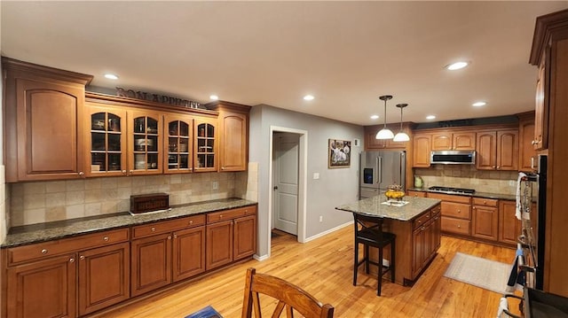 kitchen with light wood-style floors, tasteful backsplash, stainless steel appliances, and a kitchen breakfast bar