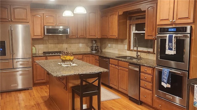 kitchen featuring a kitchen island, a sink, light wood finished floors, dark stone countertops, and stainless steel appliances