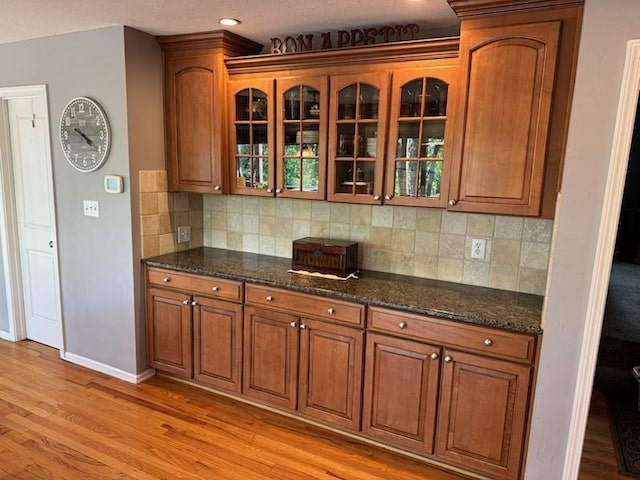 kitchen featuring brown cabinets, backsplash, glass insert cabinets, and dark stone counters