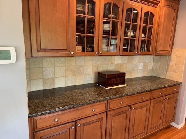 kitchen featuring brown cabinetry, dark stone countertops, and glass insert cabinets