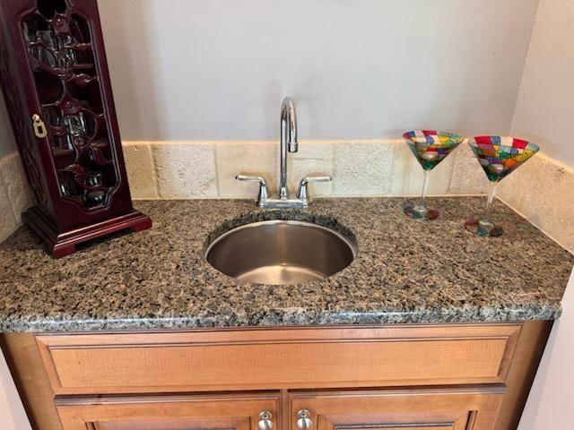 room details featuring a sink, brown cabinets, decorative backsplash, and dark stone countertops