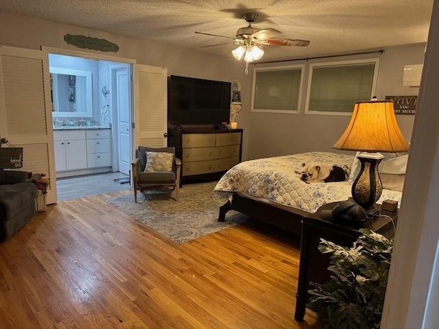 bedroom with a textured ceiling, ceiling fan, ensuite bath, and wood finished floors