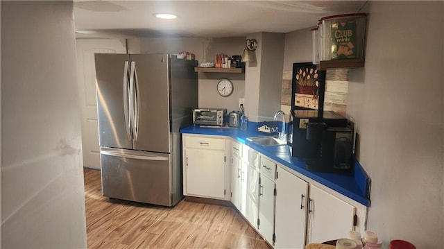 kitchen featuring open shelves, light wood-type flooring, a sink, freestanding refrigerator, and white cabinetry