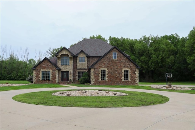 traditional-style house with curved driveway, a front lawn, and stone siding