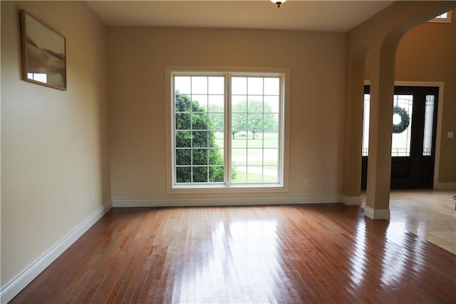 spare room featuring baseboards, arched walkways, decorative columns, and hardwood / wood-style floors