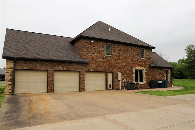 view of home's exterior with concrete driveway, brick siding, central AC, and roof with shingles