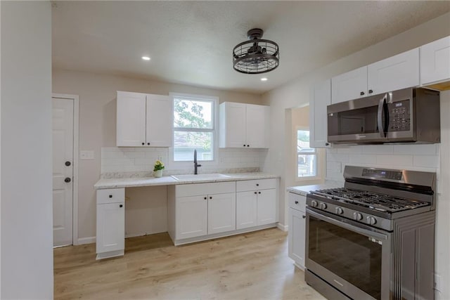 812 S Saville St, Independence, MO 64050 - kitchen featuring appliances with stainless steel finishes, a sink, light wood-type flooring, tasteful backsplash, and white cabinets