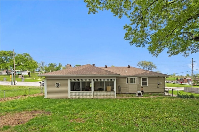 rear view of property with fence, roof with shingles, a sunroom, a chimney, and a yard
