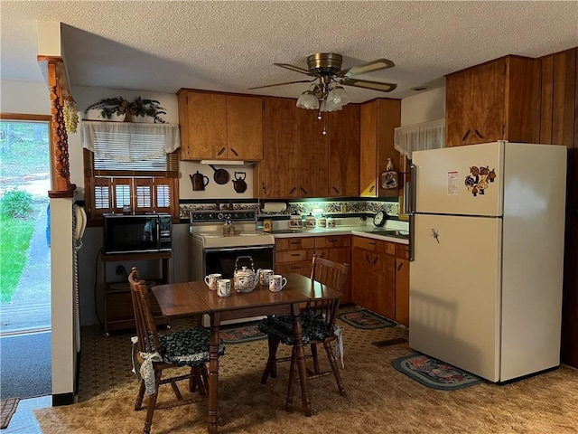 kitchen featuring ceiling fan, brown cabinetry, black microwave, freestanding refrigerator, and electric stove