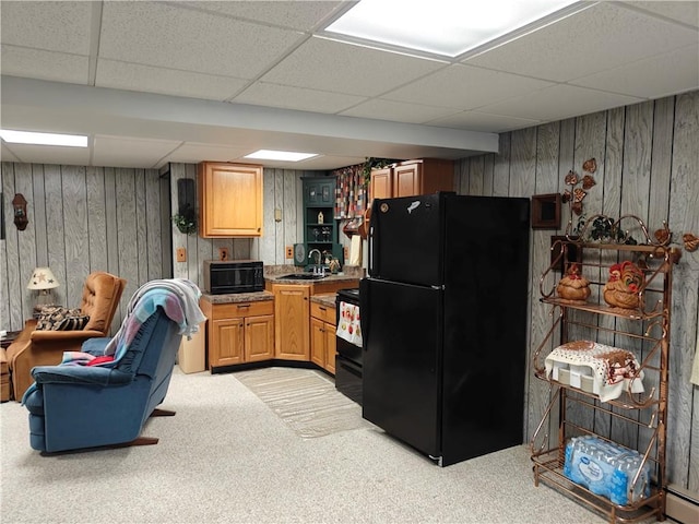 kitchen featuring light carpet, wooden walls, a paneled ceiling, a sink, and black appliances